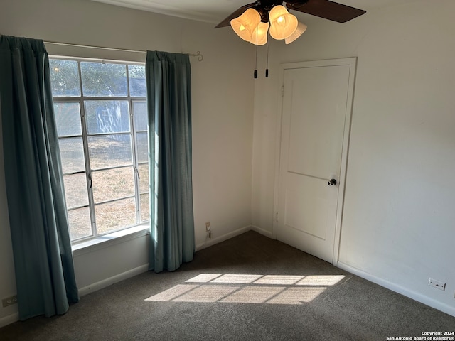 spare room featuring dark carpet, ceiling fan, and a wealth of natural light