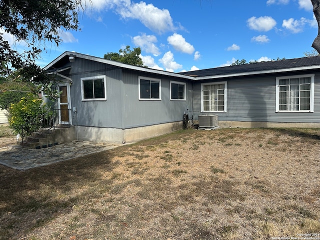 rear view of property featuring central AC unit and a lawn