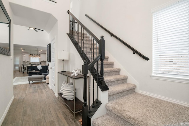 staircase with ceiling fan, baseboards, a high ceiling, and wood finished floors