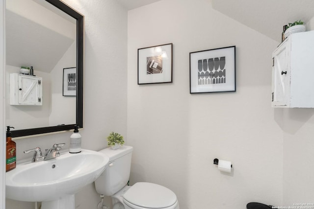 bathroom with lofted ceiling, toilet, and a sink