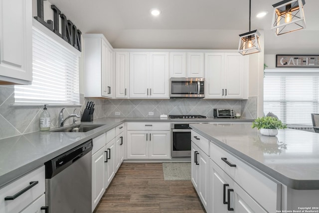 kitchen with hanging light fixtures, white cabinets, stainless steel appliances, and a sink