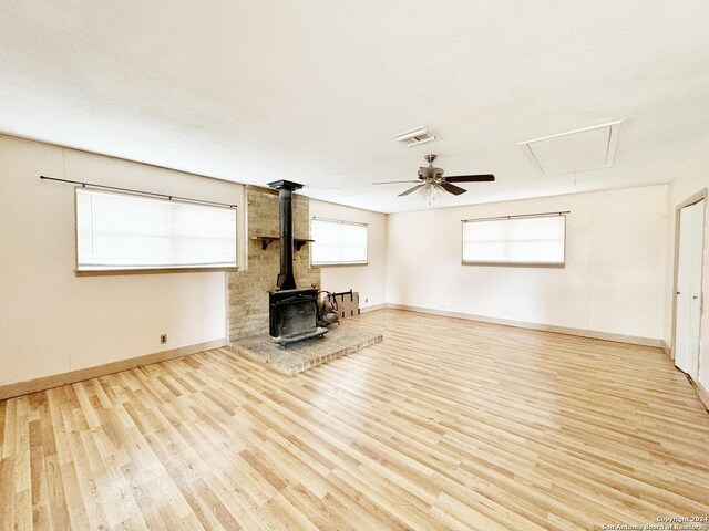 unfurnished living room with ceiling fan, a wealth of natural light, a wood stove, and light hardwood / wood-style flooring