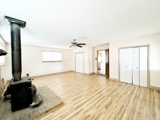 living room with a wood stove, light hardwood / wood-style flooring, and ceiling fan