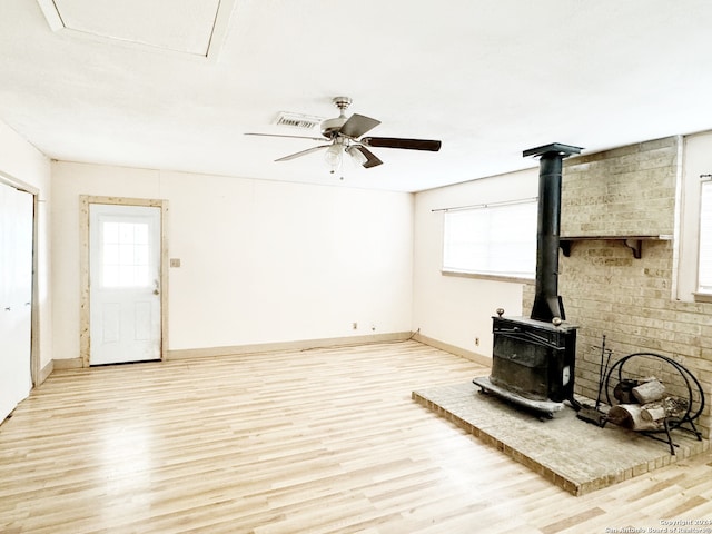 unfurnished living room with a wood stove, ceiling fan, and light hardwood / wood-style floors