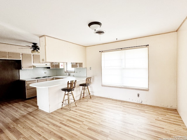 kitchen with gas stovetop, a breakfast bar, kitchen peninsula, and light wood-type flooring