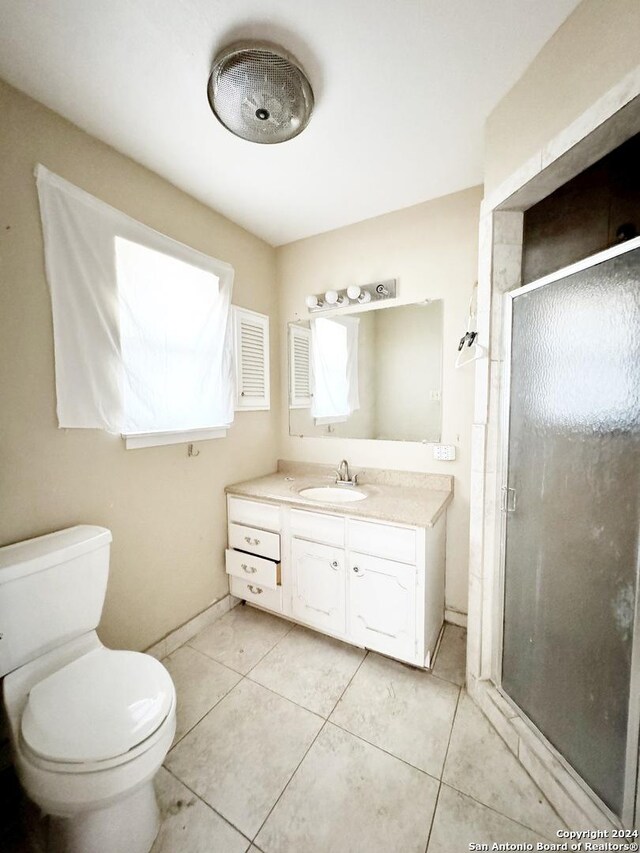 bathroom with a shower with door, vanity, toilet, and tile patterned floors