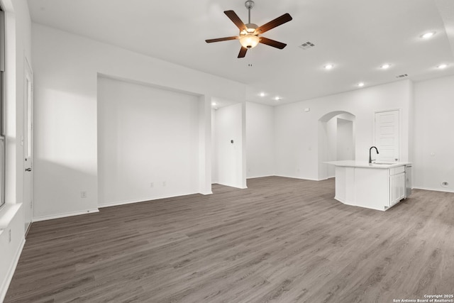 unfurnished living room with arched walkways, visible vents, ceiling fan, a sink, and wood finished floors