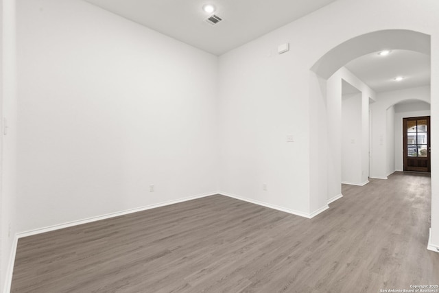 unfurnished room featuring arched walkways, recessed lighting, visible vents, wood finished floors, and baseboards