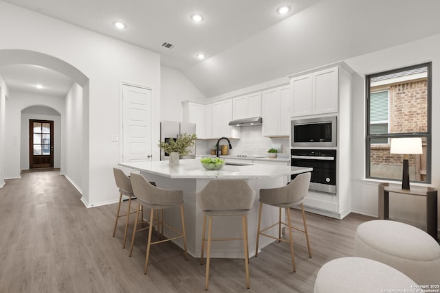 kitchen with arched walkways, visible vents, decorative backsplash, appliances with stainless steel finishes, and under cabinet range hood