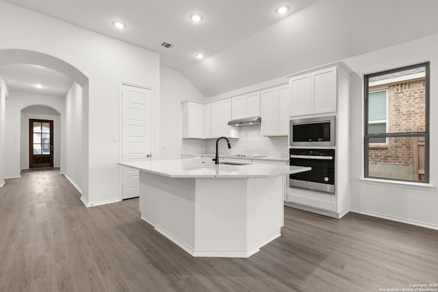 kitchen featuring arched walkways, visible vents, stainless steel microwave, wall oven, and under cabinet range hood