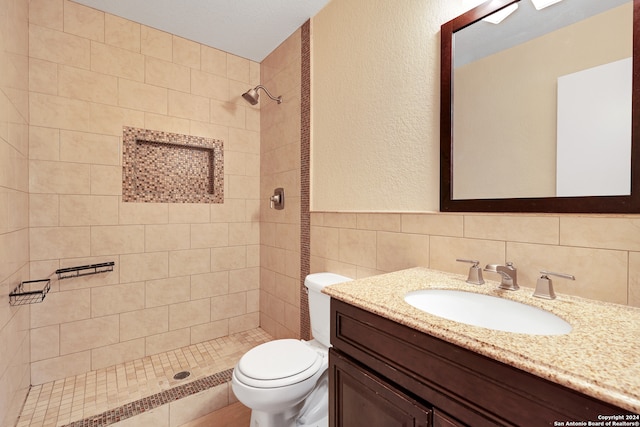 bathroom with vanity, backsplash, a tile shower, tile walls, and toilet