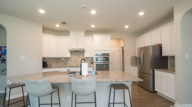 kitchen with white cabinets, appliances with stainless steel finishes, an island with sink, and decorative backsplash