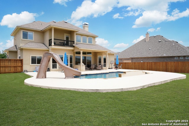 rear view of house with a lawn, a patio area, a balcony, and a fenced in pool