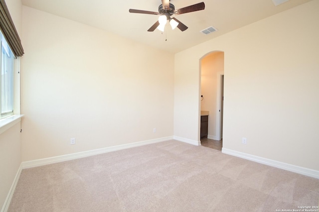 unfurnished room featuring arched walkways, visible vents, a ceiling fan, light carpet, and baseboards