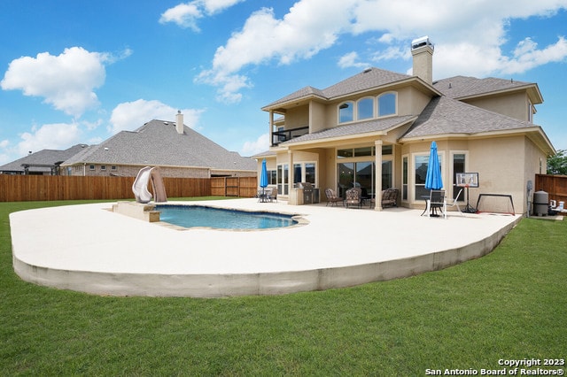 view of pool with a water slide, a lawn, and a patio area