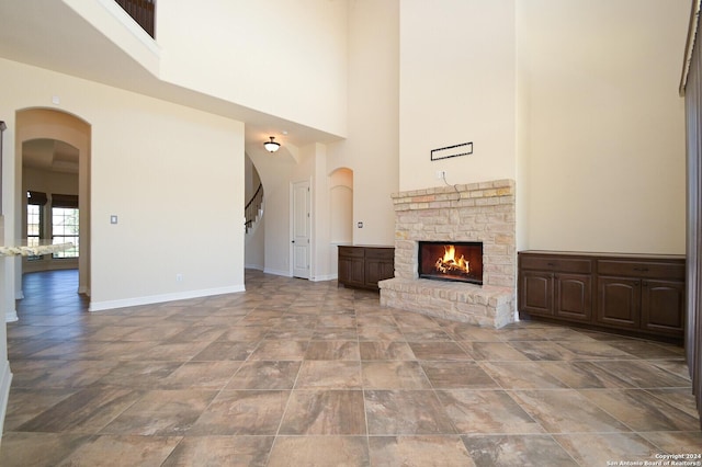 unfurnished living room with arched walkways, a lit fireplace, a high ceiling, and baseboards