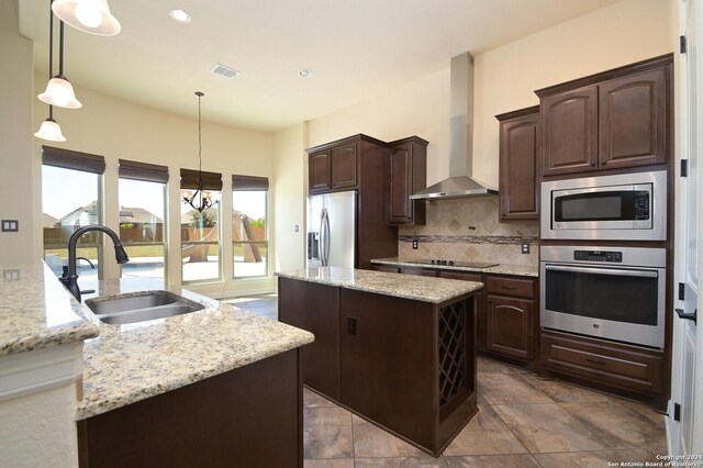 kitchen with a kitchen island, wall chimney exhaust hood, pendant lighting, appliances with stainless steel finishes, and sink