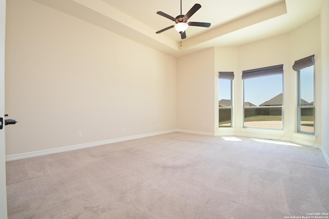 empty room with light carpet, ceiling fan, baseboards, and a raised ceiling