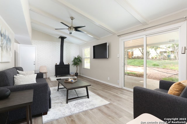 living room featuring plenty of natural light, brick wall, a wood stove, and lofted ceiling with beams