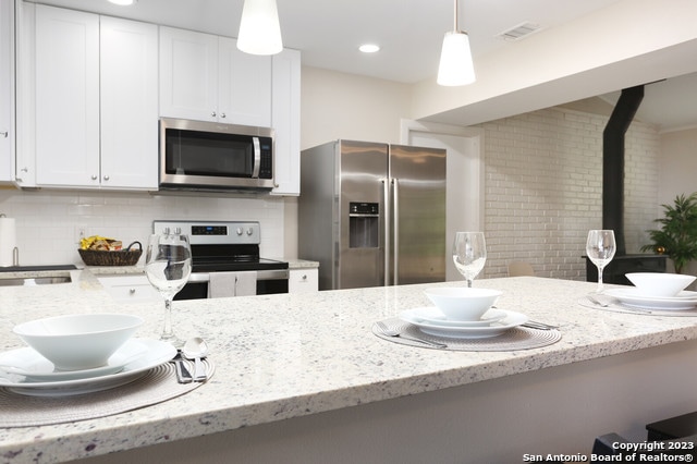 kitchen with appliances with stainless steel finishes, light stone counters, backsplash, and pendant lighting