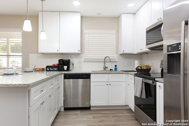 kitchen featuring light stone countertops, appliances with stainless steel finishes, sink, white cabinetry, and light wood-type flooring