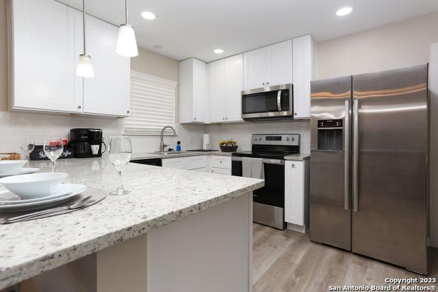 kitchen featuring backsplash, light hardwood / wood-style floors, hanging light fixtures, stainless steel appliances, and light stone counters