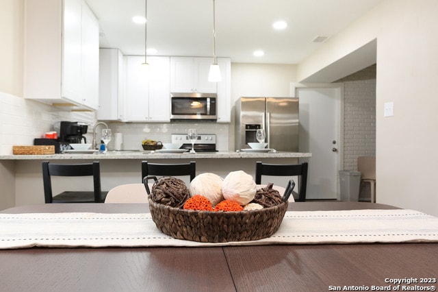 kitchen featuring appliances with stainless steel finishes, white cabinetry, a kitchen breakfast bar, and decorative backsplash