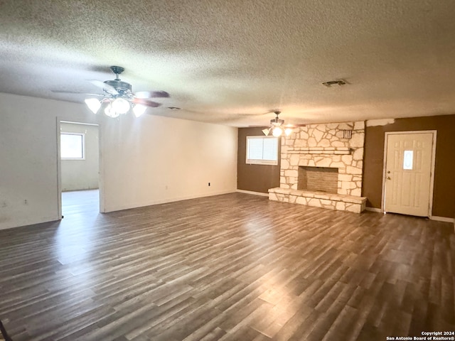 unfurnished living room featuring a textured ceiling, dark hardwood / wood-style flooring, ceiling fan, and a stone fireplace