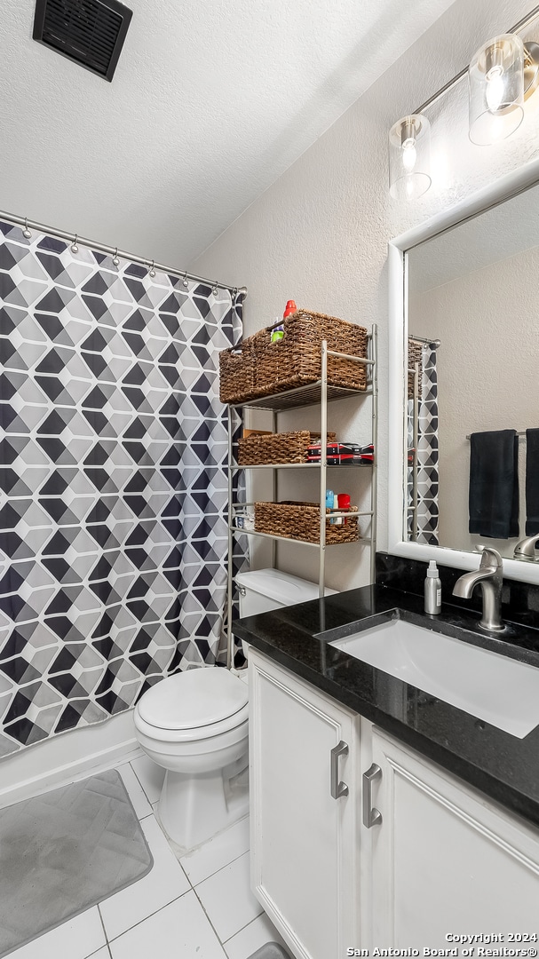 bathroom featuring toilet, tile patterned floors, vanity, a textured ceiling, and curtained shower