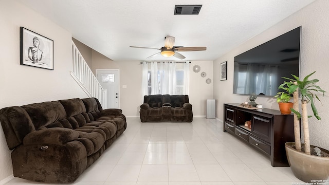 living room with ceiling fan, light tile patterned flooring, visible vents, baseboards, and stairs