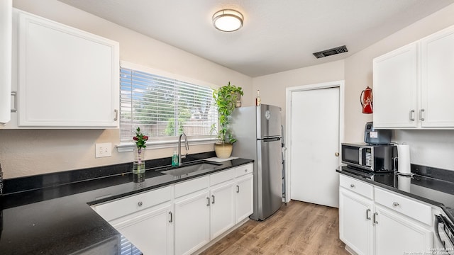 kitchen featuring dark countertops, visible vents, appliances with stainless steel finishes, white cabinetry, and a sink