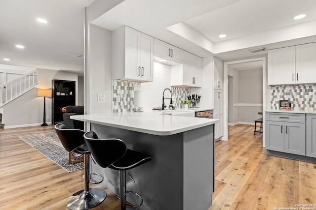 kitchen with kitchen peninsula, decorative backsplash, a kitchen breakfast bar, and light hardwood / wood-style flooring