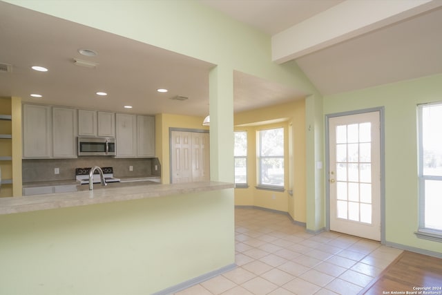 kitchen featuring backsplash, light tile patterned floors, lofted ceiling with beams, stainless steel appliances, and kitchen peninsula