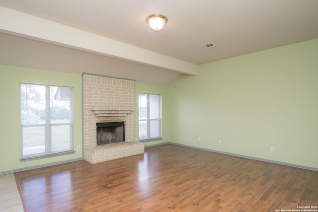 unfurnished living room featuring a brick fireplace, hardwood / wood-style floors, and beam ceiling