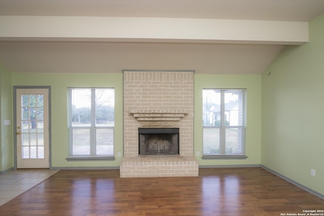 unfurnished living room with a fireplace, plenty of natural light, dark hardwood / wood-style floors, and vaulted ceiling with beams