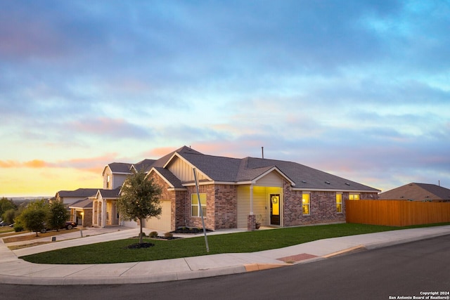 view of front of property with driveway, a lawn, an attached garage, fence, and brick siding