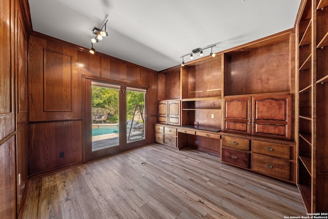 unfurnished office with rail lighting, built in desk, wooden walls, and light hardwood / wood-style flooring