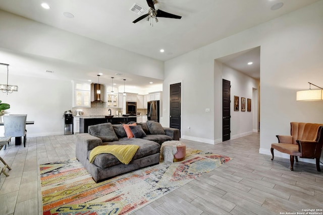 living room featuring baseboards, visible vents, light wood finished floors, and ceiling fan with notable chandelier