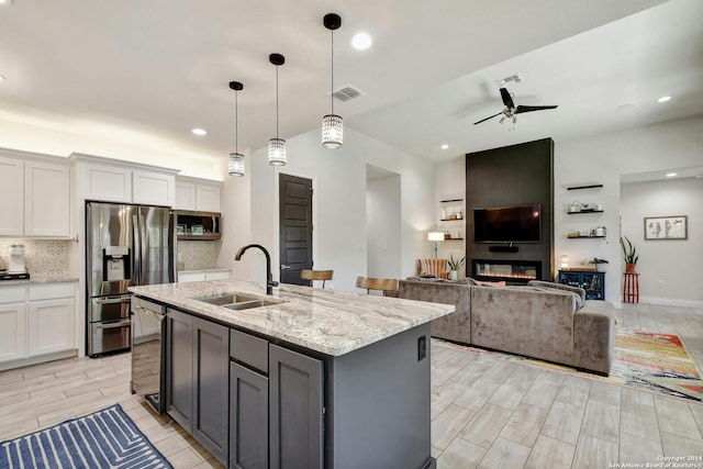 kitchen featuring a large fireplace, white cabinetry, an island with sink, ceiling fan, and sink