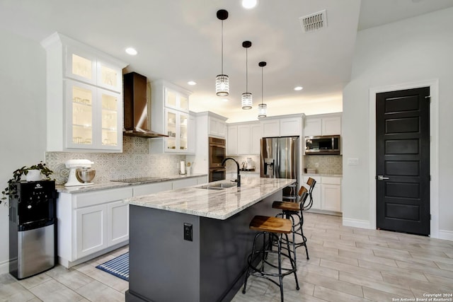 kitchen featuring appliances with stainless steel finishes, white cabinetry, wall chimney exhaust hood, a center island with sink, and tasteful backsplash