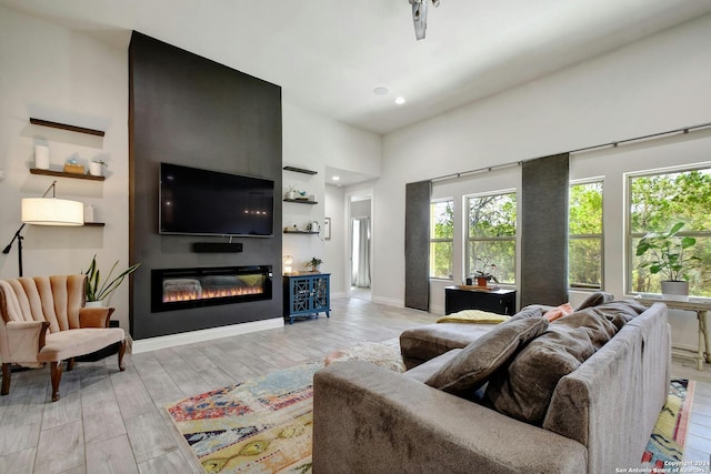 living area with light wood finished floors, recessed lighting, baseboards, and a glass covered fireplace