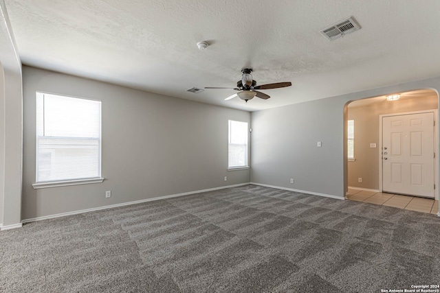 carpeted empty room featuring a wealth of natural light, ceiling fan, and a textured ceiling