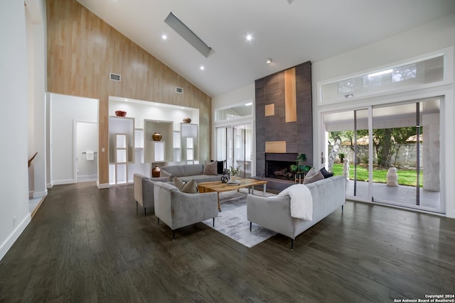 living area featuring visible vents, dark wood finished floors, a fireplace, a skylight, and high vaulted ceiling