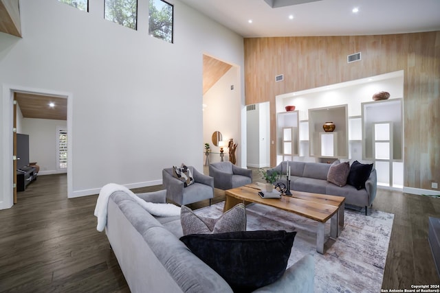 living room featuring baseboards, visible vents, high vaulted ceiling, dark wood-type flooring, and wood walls