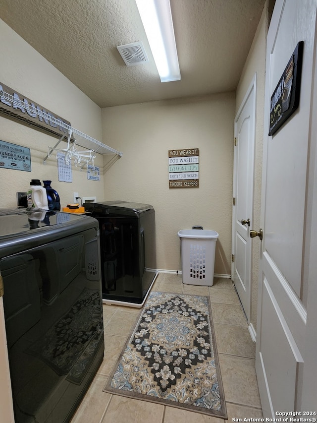 laundry area featuring a textured ceiling, light tile patterned flooring, and washing machine and clothes dryer