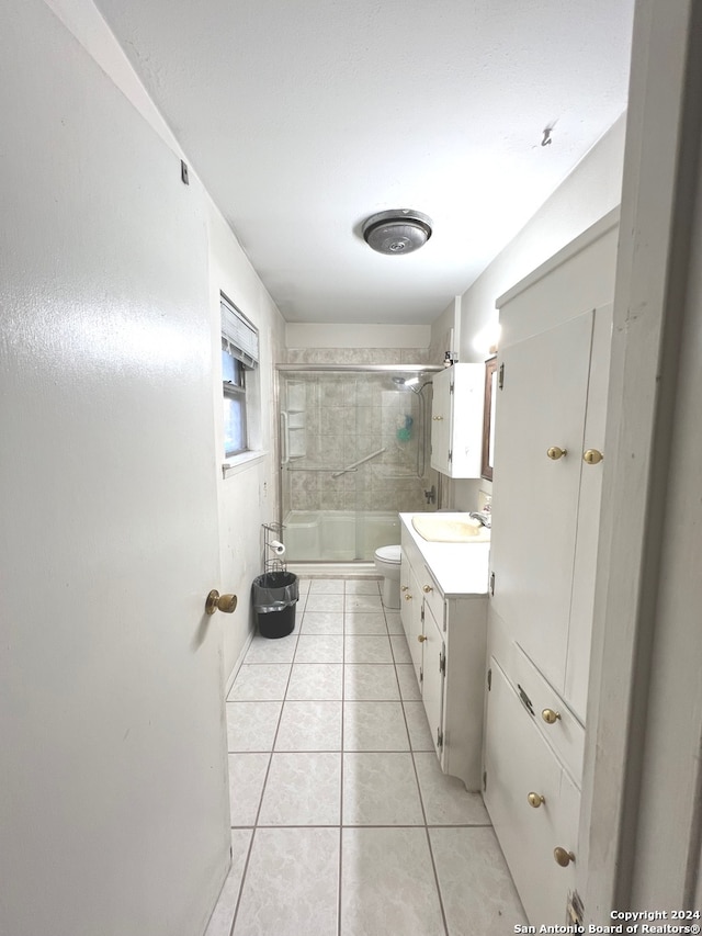 bathroom with a shower with door, vanity, toilet, and tile patterned floors