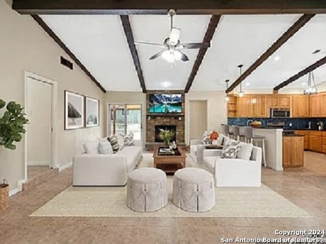 living room with ceiling fan, a stone fireplace, and lofted ceiling with beams