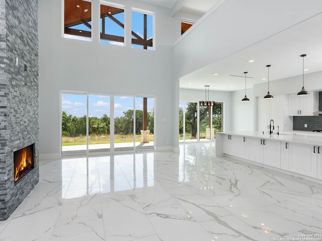 unfurnished living room featuring a stone fireplace, a towering ceiling, sink, and a wealth of natural light