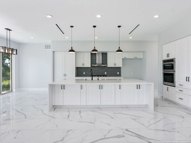 kitchen with pendant lighting, a center island with sink, wall chimney range hood, decorative backsplash, and double oven