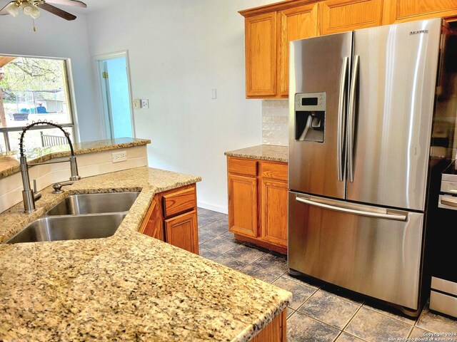 kitchen featuring stainless steel fridge, light stone countertops, sink, decorative backsplash, and ceiling fan